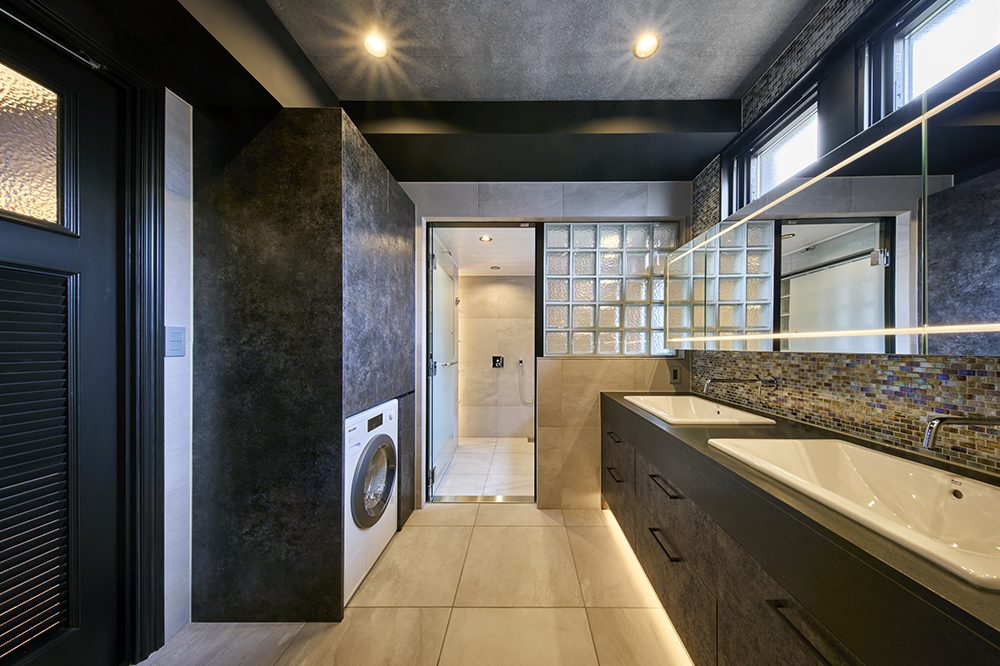 間接照明を施したツインボウルの洗面。造作の浴室が続きます。